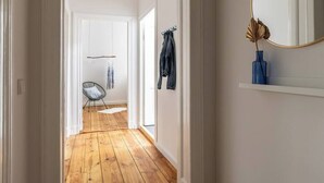 Een gang met houten vloer, een stoel, een kapstok en een spiegel aan de muur.