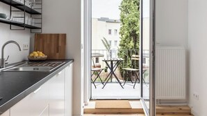Een moderne keuken met een inbouwspoelbak, een houten snijplank en een schaal met citroenen. Een glazen deur leidt naar een buiten zitgedeelte met een tafel en stoelen.