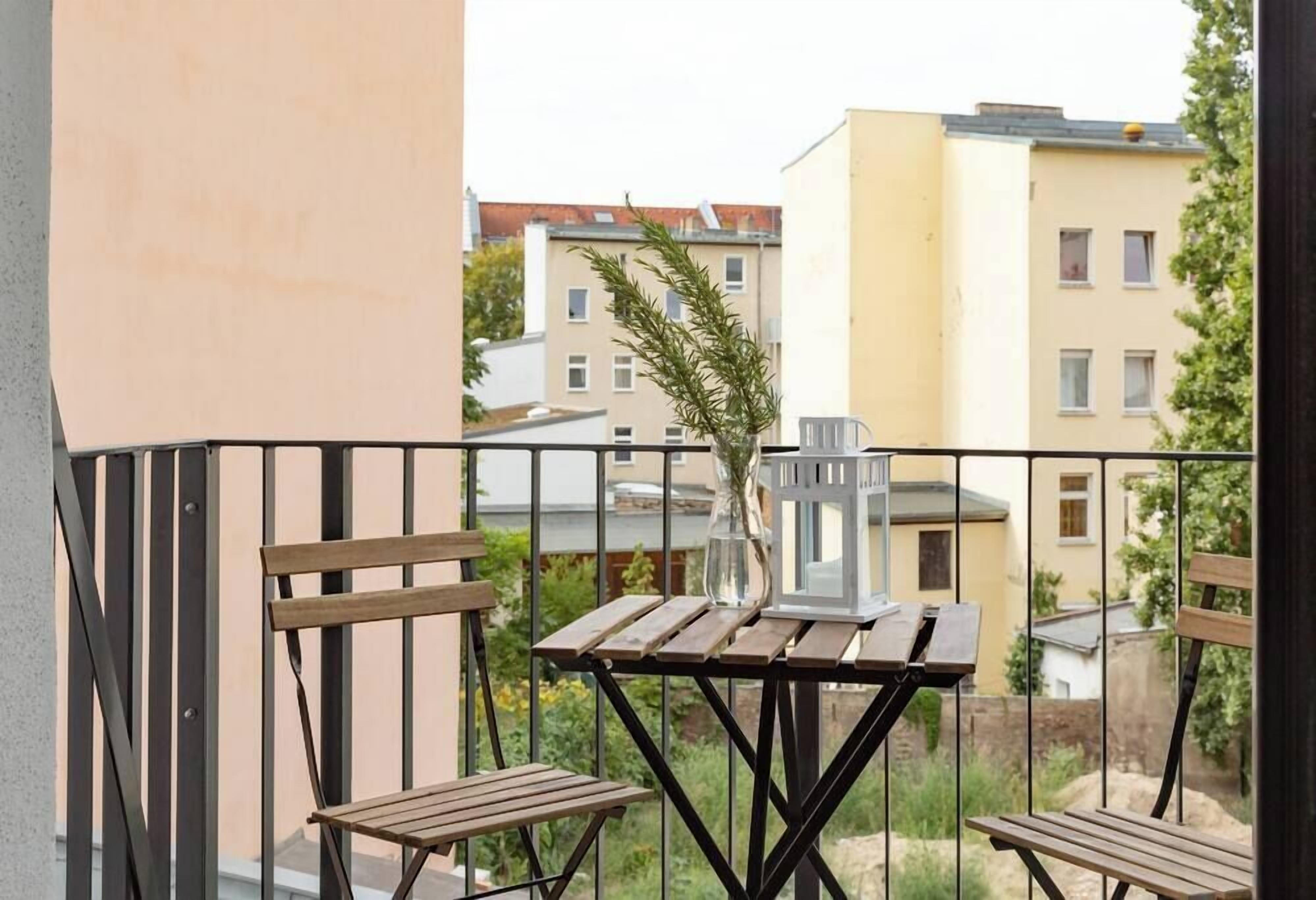 A balcony with two wooden chairs and a small table, a potted plant, and a white lantern.