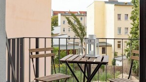 Een balkon met twee houten stoelen, een kleine tafel, een bloempot en een witte lantaarn.