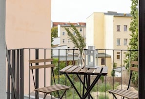 A balcony with a wooden table and chairs, a vase with a plant, and a lantern.
