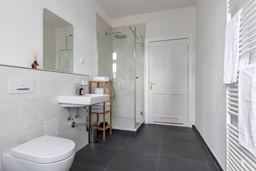 Ein modernes Badezimmer mit Toilette, Waschbecken, einer Duschkabine aus Glas und einer weißen Tür.