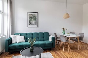 A living room with a teal sofa, a round coffee table, and a dining area with a table and chairs.