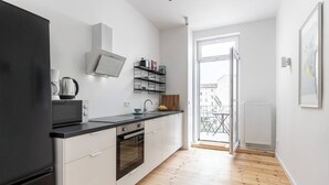 Eine moderne Küche mit weißen Schränken, einer schwarzen Arbeitsplatte und einem eingebauten Backofen. Ein Fenster bietet Blick auf einen Balkon.