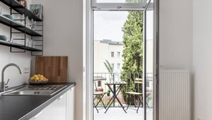 Eine moderne Küche mit integriertem Spülbecken, einem Holztisch und einer Zitronenschale. Sie öffnet sich zu einem Außenbereich mit Tisch und Stühlen, Blick auf ein Gebäude und einen Baum.