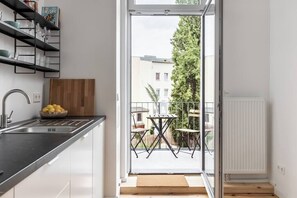 Cozinha moderna com pia embutida, tábua de corte de madeira e um recipiente com limões. Dá acesso a uma área externa com mesa e cadeiras, vista de um edifício e uma árvore.