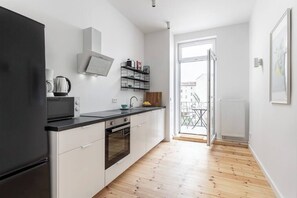 Cozinha moderna com armários brancos, bancada preta e forno embutido. Há uma janela com vista para uma varanda.