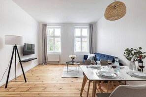 Uma sala de estar moderna com área de jantar, janelas amplas, um sofá azul e uma mesa posta para refeições.