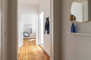 Um corredor com piso de madeira, uma cadeira, um porta-roupas e um espelho na parede.
