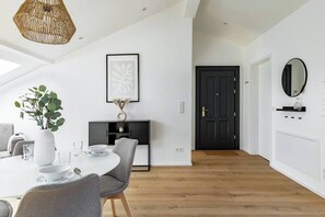 Un área de comedor moderna con una mesa redonda, sillas grises, un jarrón blanco con una planta y un mueble negro con estantes.