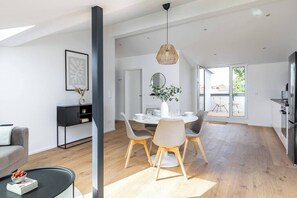 Una sala de estar moderna con comedor, que incluye una mesa redonda, sillas y una lámpara colgante.