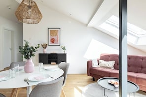 A modern living room with a dining area, a pink sofa, and a ceiling skylight.