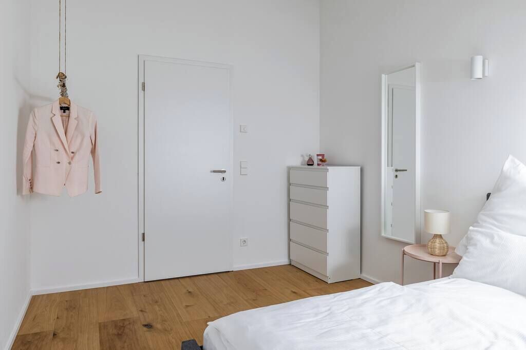 Une chambre à coucher au style minimaliste, avec un lit, une commode, une armoire et un manteau suspendu.