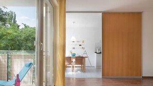 A modern interior with a wooden floor, a dining area with a table and chairs, and a view of greenery outside. - 65 m² Apartment w. Spreeview directly at Ostkreuz (Berlin)