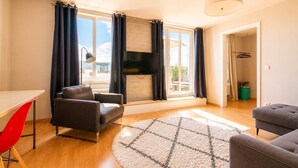 A modern living room with a sofa, a red chair, a TV, and a large window with curtains.