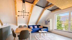 A loft-style room with a dining table, chairs, a sofa, and a large window with a view. - Bright Hideaway (70 sqm) near BER Airport (Berlin)