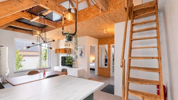 A modern kitchen with a marble countertop, wooden ceiling beams, and a wooden ladder. - Bright Hideaway (70 sqm) near BER Airport (Berlin)
