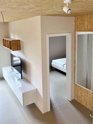 A modern room with a built-in TV, a wooden shelf, a bed, and a large mirror.