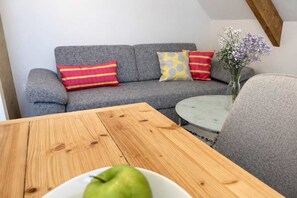 A grey sofa with striped pillows, a round coffee table, and a vase with flowers.