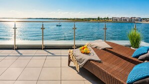 A terrace with a view of the sea, a lounge area with a woven sofa, a bowl of fruit, and a railing. - "Sky 65" - Exclusive penthouse with sauna & sea view at Ostsee Resort Olpenitz (Ostseeresort Olpenitz)