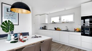 A modern kitchen with white cabinets, a black and gold pendant light, a dining table with chairs, and a window above the sink. - "Sky 65" - Exclusive penthouse with sauna & sea view at Ostsee Resort Olpenitz (Ostseeresort Olpenitz)