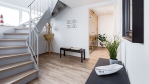 A modern interior with a staircase, a wall-mounted text, a small table, a potted plant, and a decorative boat on a console table. - "Sky 65" - Exclusive penthouse with sauna & sea view at Ostsee Resort Olpenitz (Ostseeresort Olpenitz)