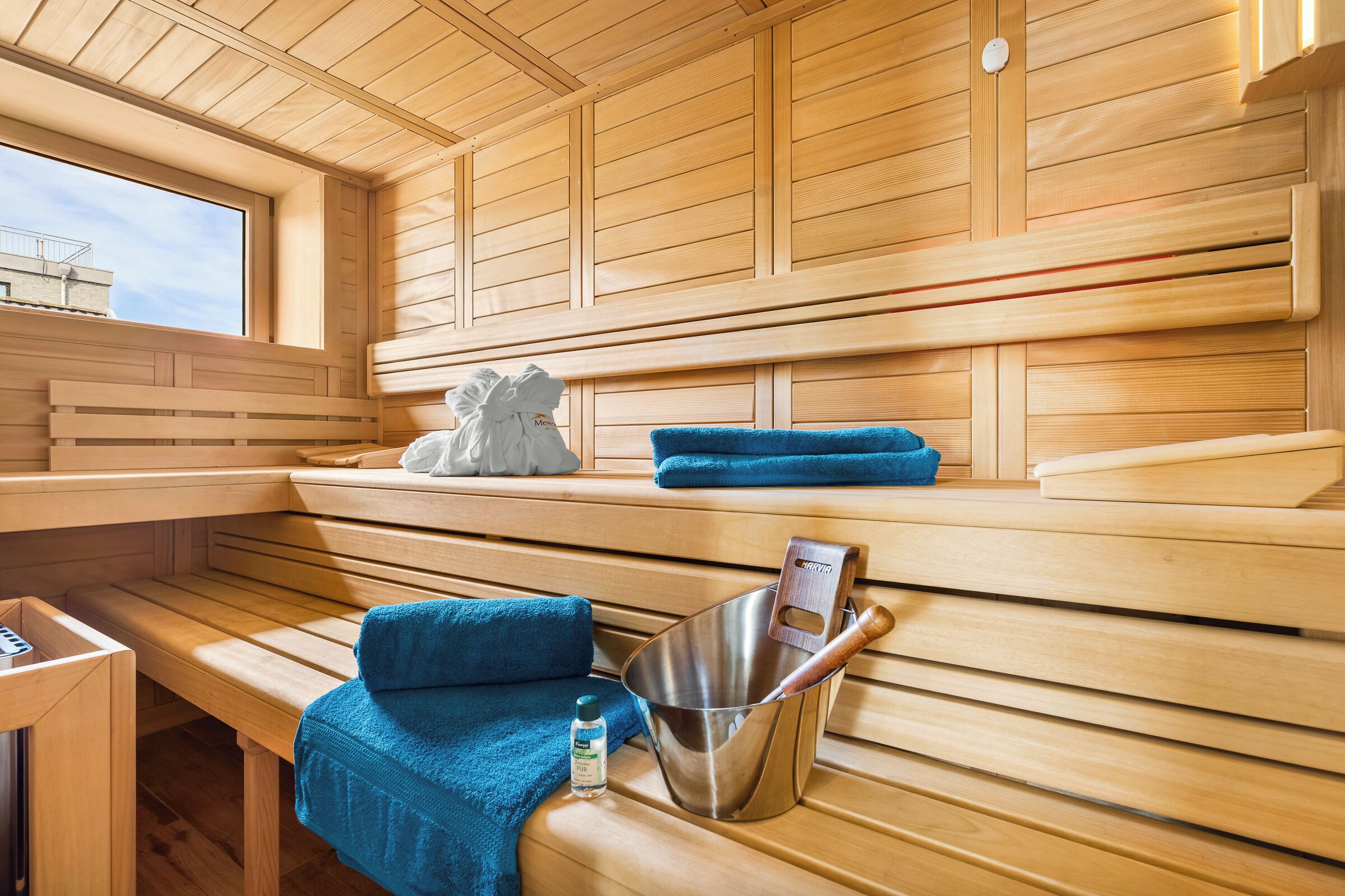 A sauna with wooden benches, a metal bucket, and a towel.
