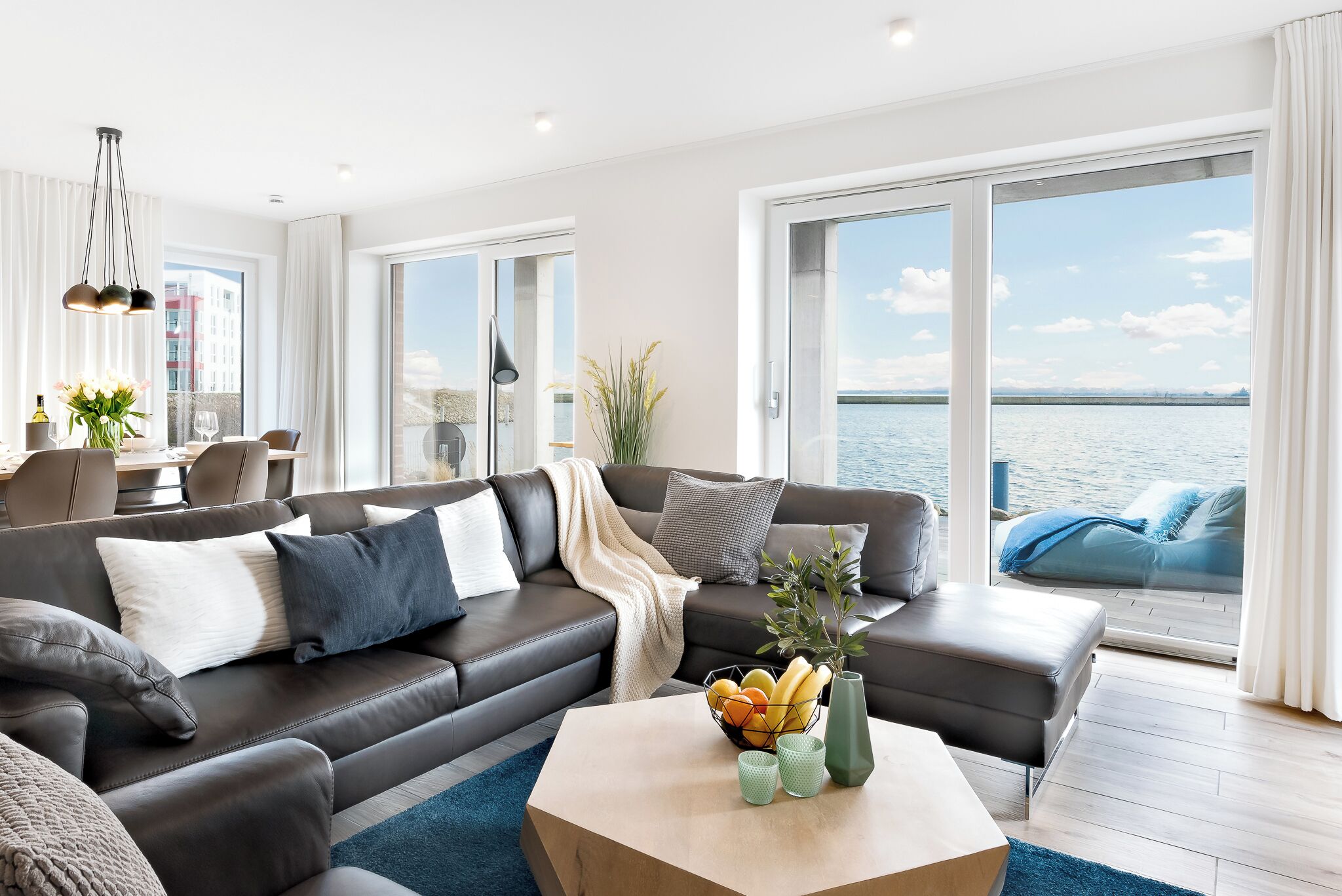 Een moderne woonkamer met een leren bank, een bijzettafeltje met fruit en uitzicht op zee.