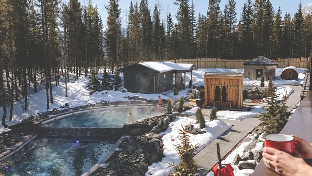 Ein Resort mit Thermalquelle, Holzhütten und verschneiteter Waldkulisse.