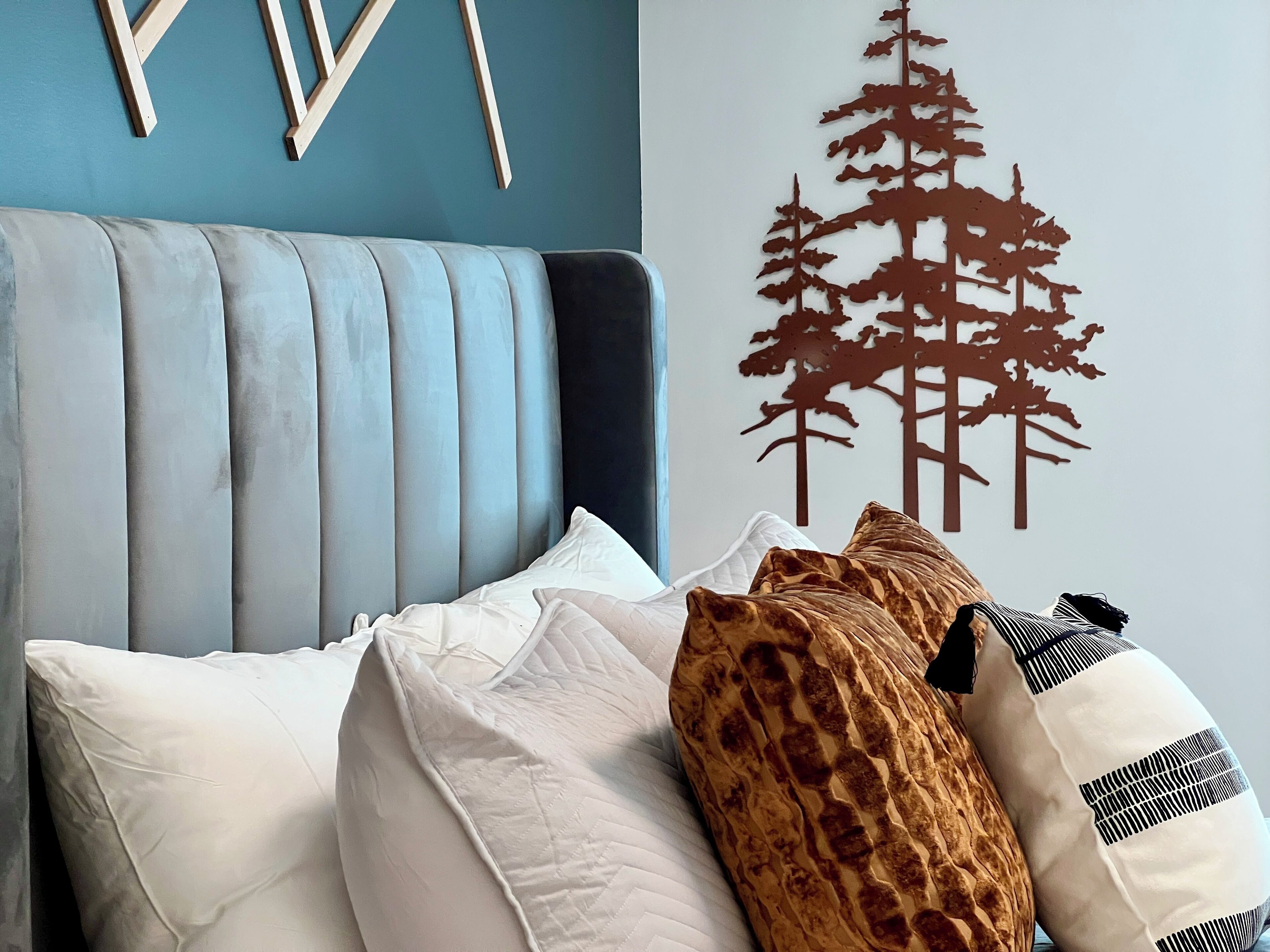 A bedroom with a tufted headboard, a bed with white and patterned pillows, and a wall with a tree decal.