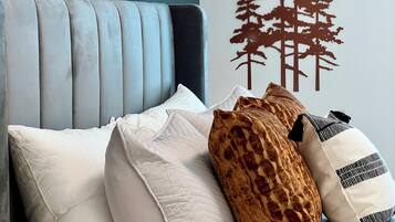 A bedroom with a tufted headboard, a bed with white and patterned pillows, and a wall with a tree decal.