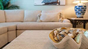 Een woonkamer met een beige bank, een bijzettafeltje en een schaal met schelpen.