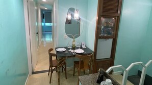 Un petit coin repas avec une table pour deux, un miroir au-dessus de la table et un coin cuisine équipé d’une cuisinière et d’un évier.