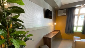 Un salon moderne agrémenté d’une grande plante, d’un banc en bois et d’un téléviseur fixé sur un mur à texture.