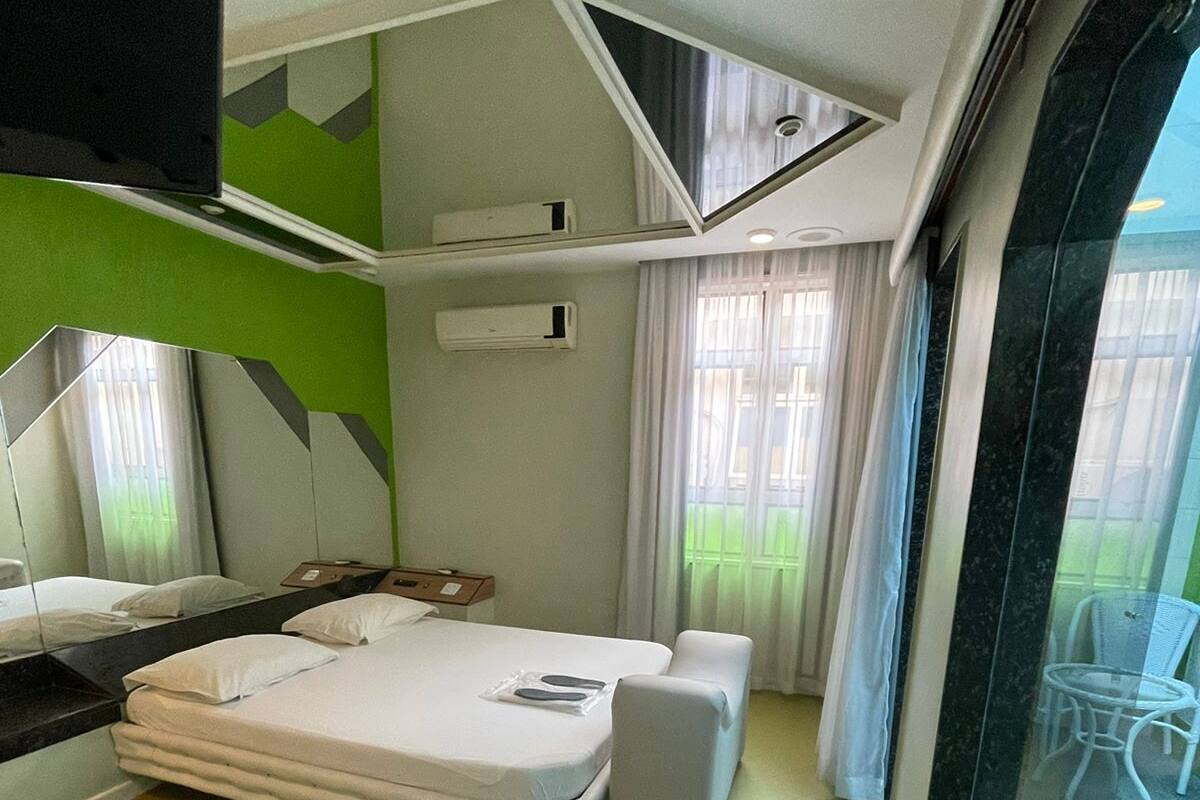 Habitación de hotel compacta con cama, un pequeño rincón de descanso, kitchenette y un amplio ventanal con vistas al exterior.