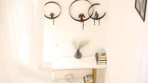 A room with a white marble wall, a shelf with books and a vase, and three wall-mounted circular decorations with hanging figures.