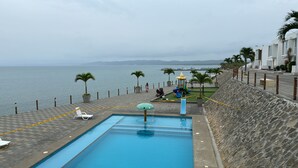 A swimming pool with a view of the sea, a children's play area, and a stone wall.