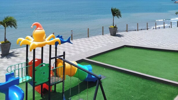 A playground with slides and swings, a paved area, and a view of the sea.