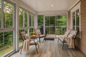 A sunroom with large windows, a wooden floor, and a seating area with chairs and a table.