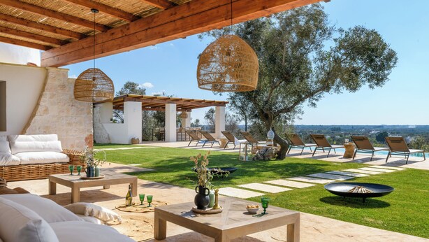 An outdoor patio with wicker furniture, a stone table, and a view of the landscape. - Villa Pajaro Ostuni Piscina a Sfioro e Vista Panoramica (Puglia)