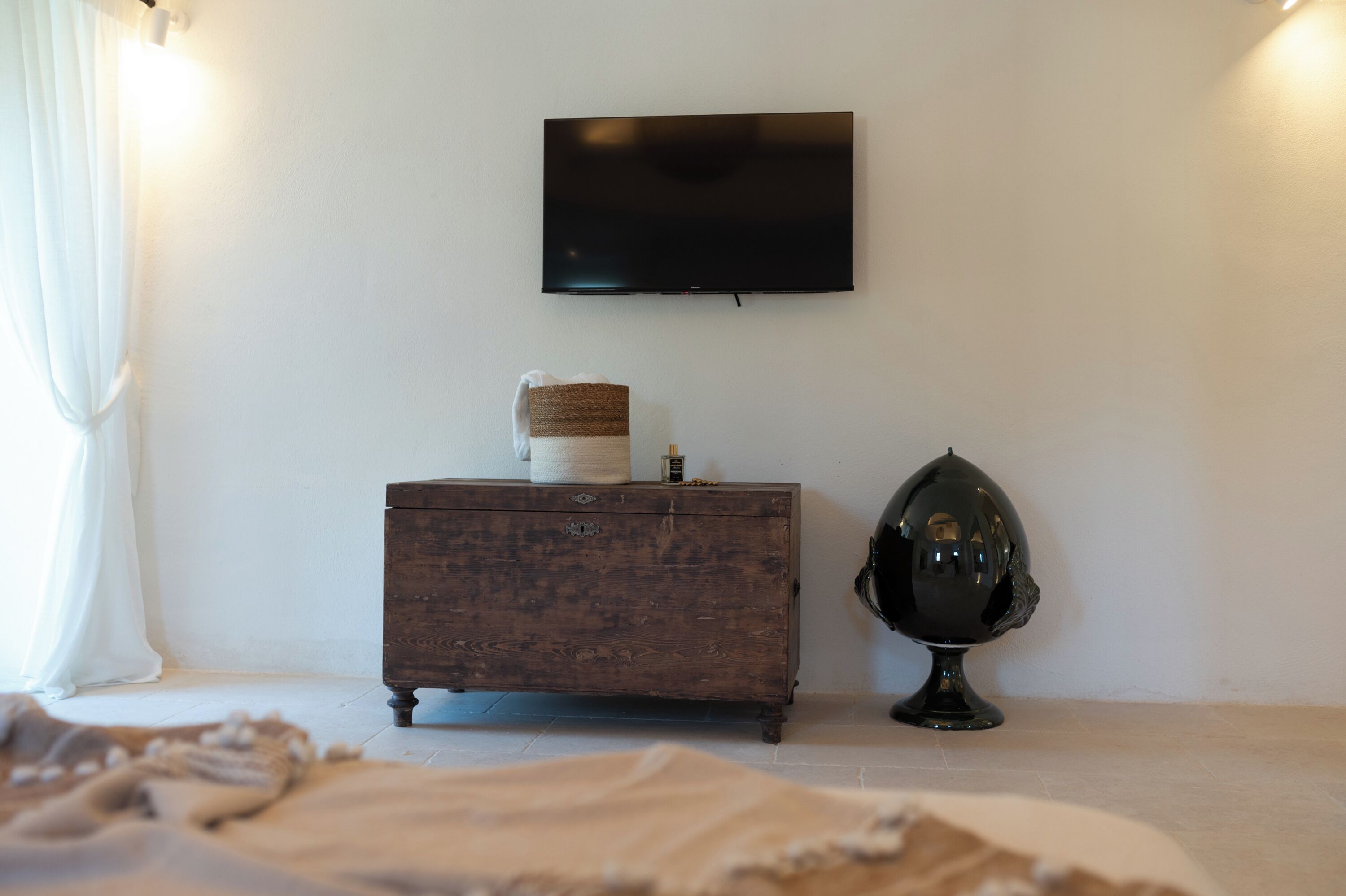 Quarto com cômoda de madeira, televisão na parede e um globo decorativo.