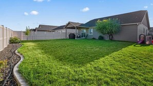 A residential backyard with a well-maintained lawn, a wooden fence, and a house with a garage and a covered porch.