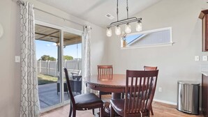 A dining area with a round table and chairs, a hanging light fixture, and a sliding glass door leading to an outdoor patio.