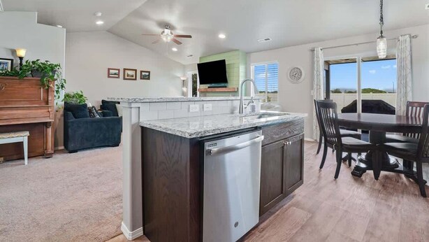 A modern kitchen with a built-in dishwasher, a dining area with a dark wooden table and chairs, and a ceiling fan.