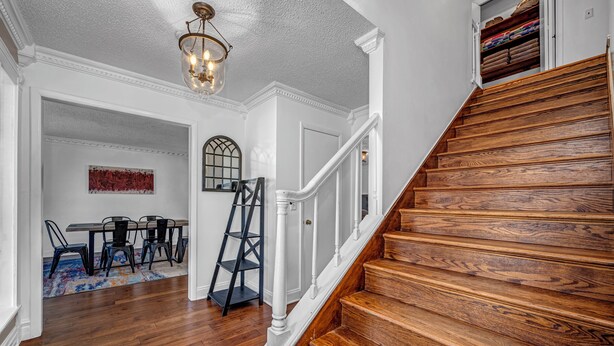 A staircase with wooden steps and white railings leading to a room with a dining area, a ladder, and a chandelier.