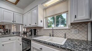 A kitchen with white cabinets, granite countertops, a double sink, and a window with blinds.