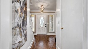 A hallway with a wooden floor, white walls, and a decorative door with a glass panel.