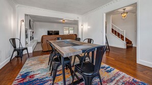 A dining area with a wooden table, black chairs, and a colorful rug. There is a staircase leading to another room.