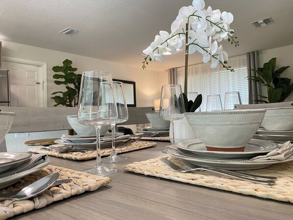 A dining table set with clear glassware, white bowls, and woven placemats.