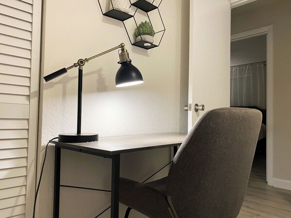 Un escritorio con una lámpara de mesa negra, una silla gris y un estante hexagonal con una planta.